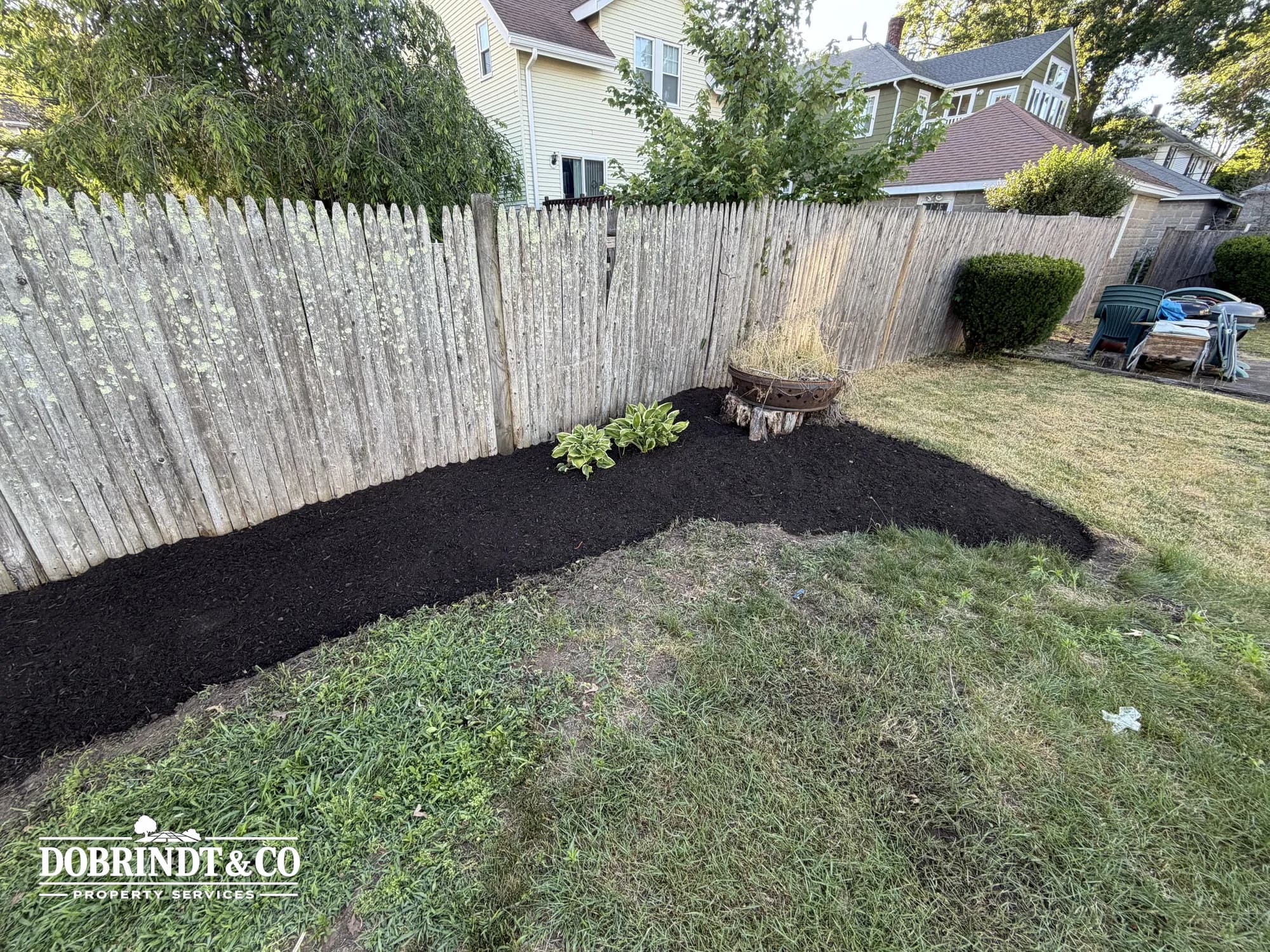 Landscaped backyard with a freshly mulched garden bed and a cluster of potted plants beside a wooden fence.