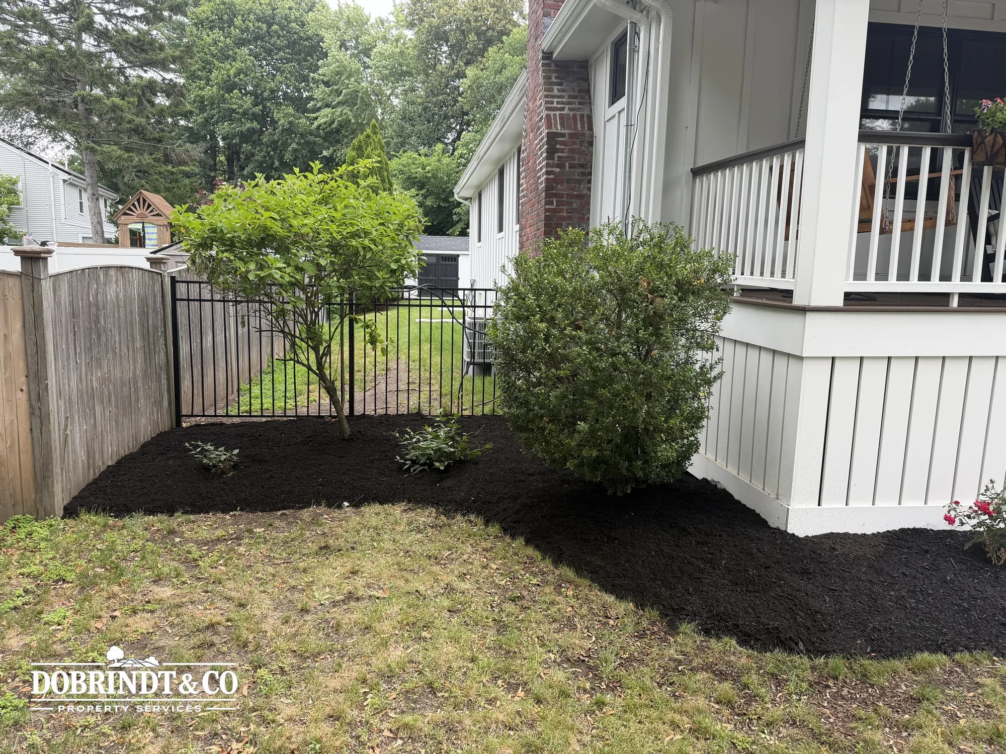 Landscaped area alongside a home with freshly mulched soil and small new plantings near a porch.