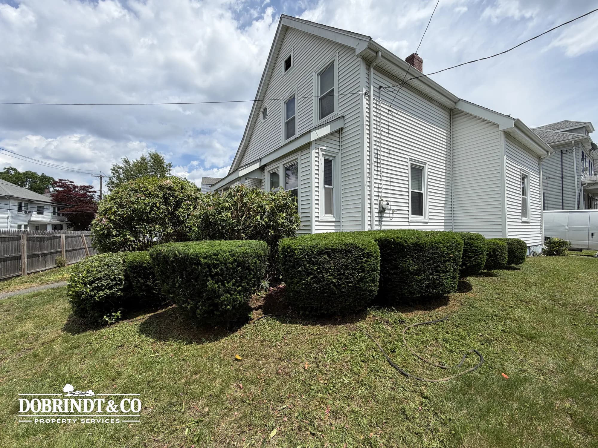 Residential property with a white exterior and neatly trimmed bushes on a green lawn under a clear sky.